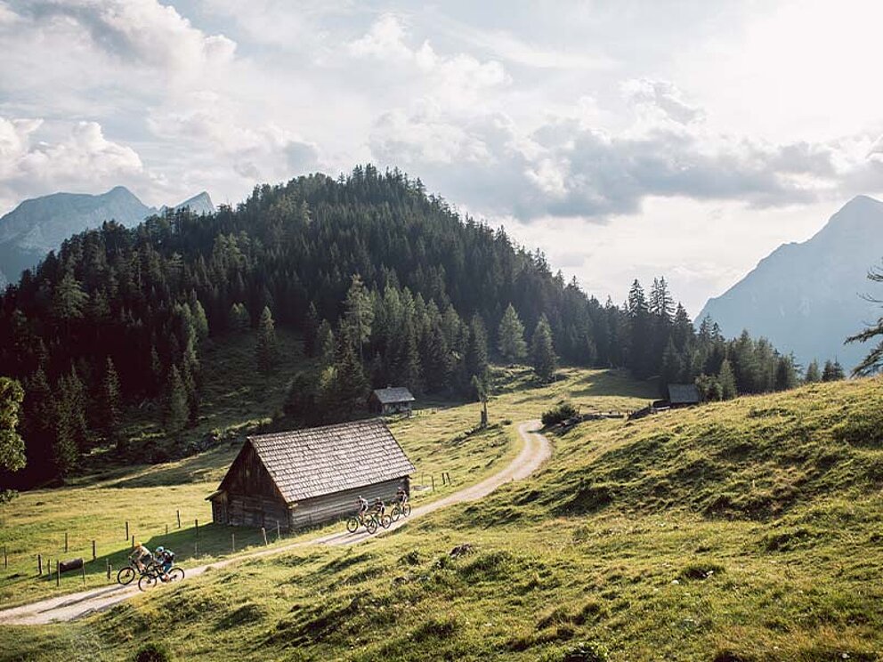 ein Schotterweg mit Bikern, eine Hütte und Berge im Hintergrund
