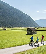 3 Radfahrer stehend am asphaltierten ebenen Radweg, im Hintergrund Berge
