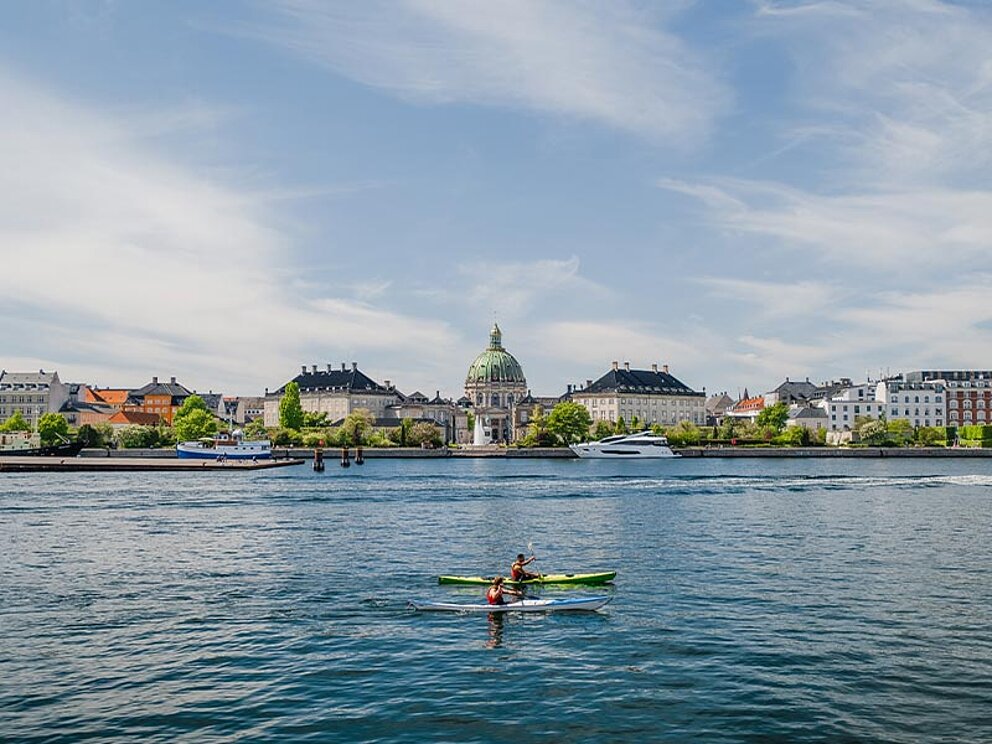 Blick auf die Stadt vom Wasser aus, im Vordergrund 2 Ruderer im Ruderboot