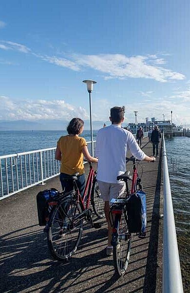 Zwei Radfahrer stehen auf einem Steg und blicken auf den Bodensee