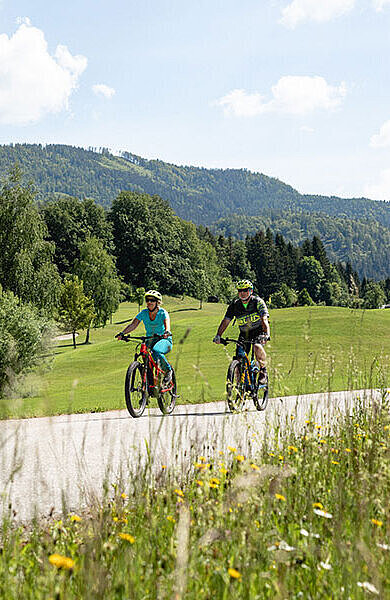 Paar auf E-Bikes am Radweg umgeben von Hügeln und Wiesen