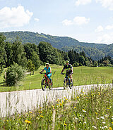 Paar auf E-Bikes am Radweg umgeben von Hügeln und Wiesen