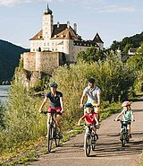 Eltern und Kinder radeln am Radweg vor Schloss Schönbühel