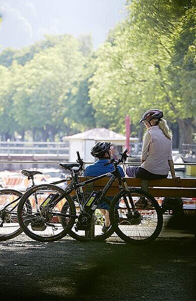 2 Radfahrer auf einer Parkbank am Bodensee-Ufer