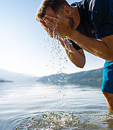 ein Mann bis zu den Knien im See wäscht sich das Gesicht
