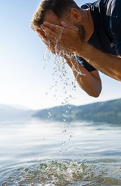 ein Mann bis zu den Knien im See wäscht sich das Gesicht
