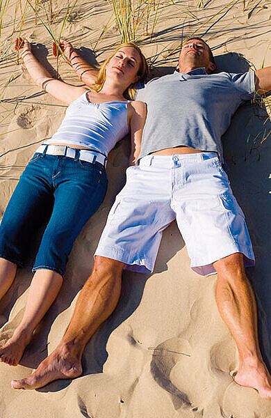 Junges Paar im Sand am Strand liegend direkt vor einer Düne