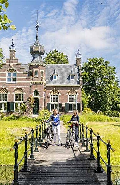 2 Damen mit Fahrrad auf einer Brücke, im Hintergrund ein kleines Schloss