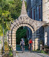 2 Radfahrer fahren durch ein steinernes Tor