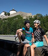 ein Paar auf einer Steinmauer, im Hintergrund die Festung Kufstein