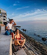 2 Personen auf großen Sitzstufen an der Adria Küste, daneben ein Fahrrad