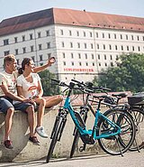 Zwei E- Biker machen Pause am Donauradweg - im Hintergrund das Schloss Linz