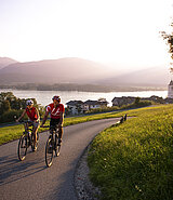 2 cyclists cycle into the sunset of Lake Wolfgangsee