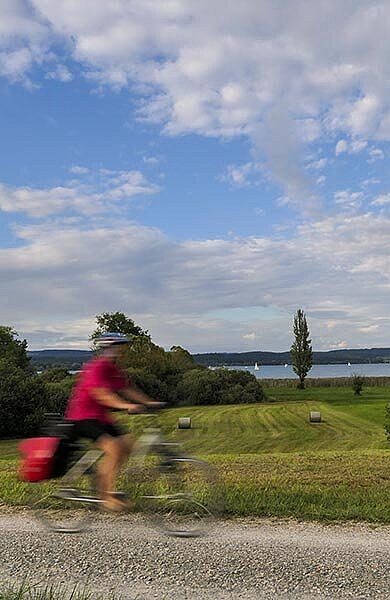 Ein Radfahrer im Schotterweg, im Hintergrund der Bodensee