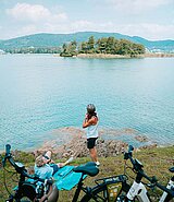 2 Personen am Ufer des Wörthersees, im Vordergrund ihre E-Bikes, im Hintergrund eine Insel im See