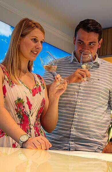 Mann und Frau verkosten Frankenwein. Sie halten Weingläser in den Händen, Bocksbeutelflaschen stehen davor.